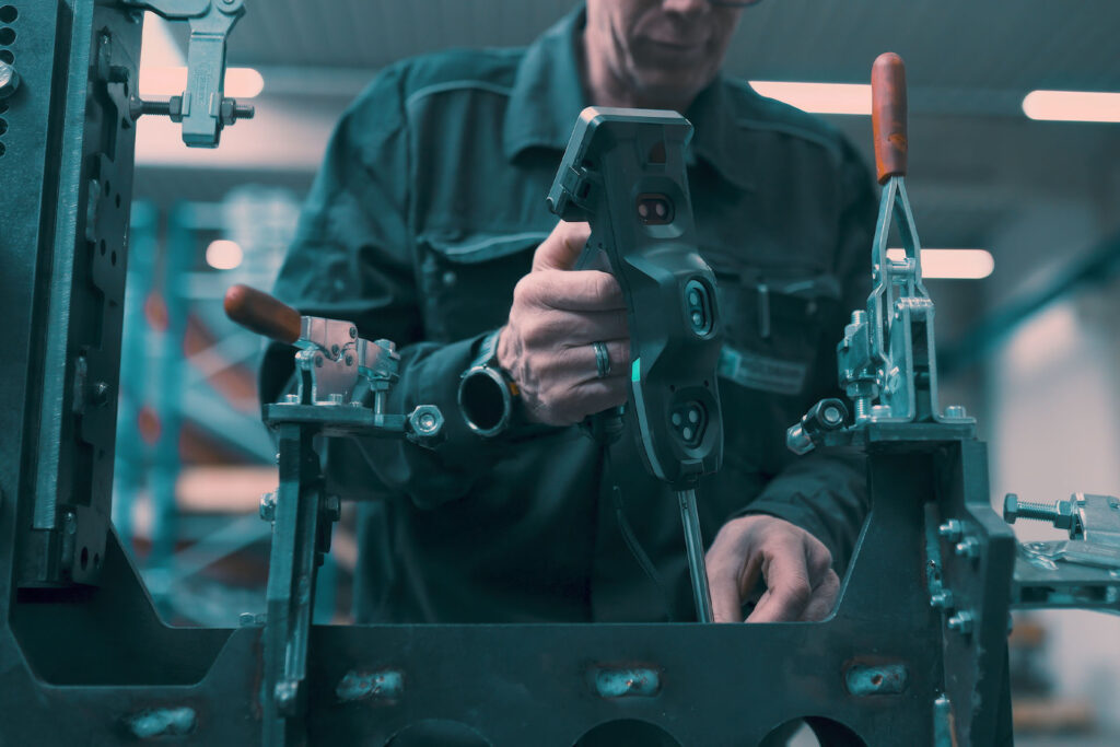 Mitarbeiter prüft ein Metallbauteil mit einem Messgerät